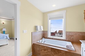 Ein Badezimmer mit einer großen Badewanne, einem Fenster mit Blick und einem Bett im angrenzenden Zimmer.