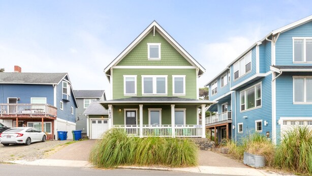 A two-story house with a green front and white trim, a porch with a railing, and a garage.