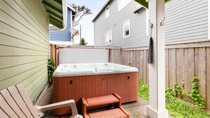 A backyard with a hot tub, wooden deck, and two chairs.