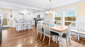 A spacious kitchen with white cabinetry, a wooden dining table, and a large window providing natural light.