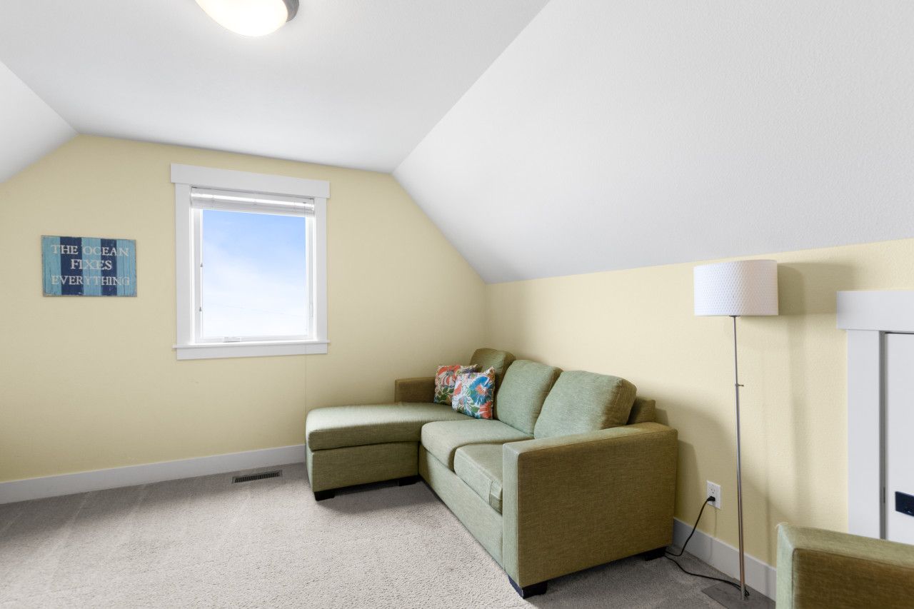 Una habitación con un sofá seccional verde, una ventana, una lámpara de pie y un letrero en la pared.