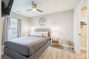 Une chambre à coucher comprenant un lit, un ventilateur de plafond, une œuvre d’art accrochée au mur, des lampes de chevet et une fenêtre avec des rideaux.