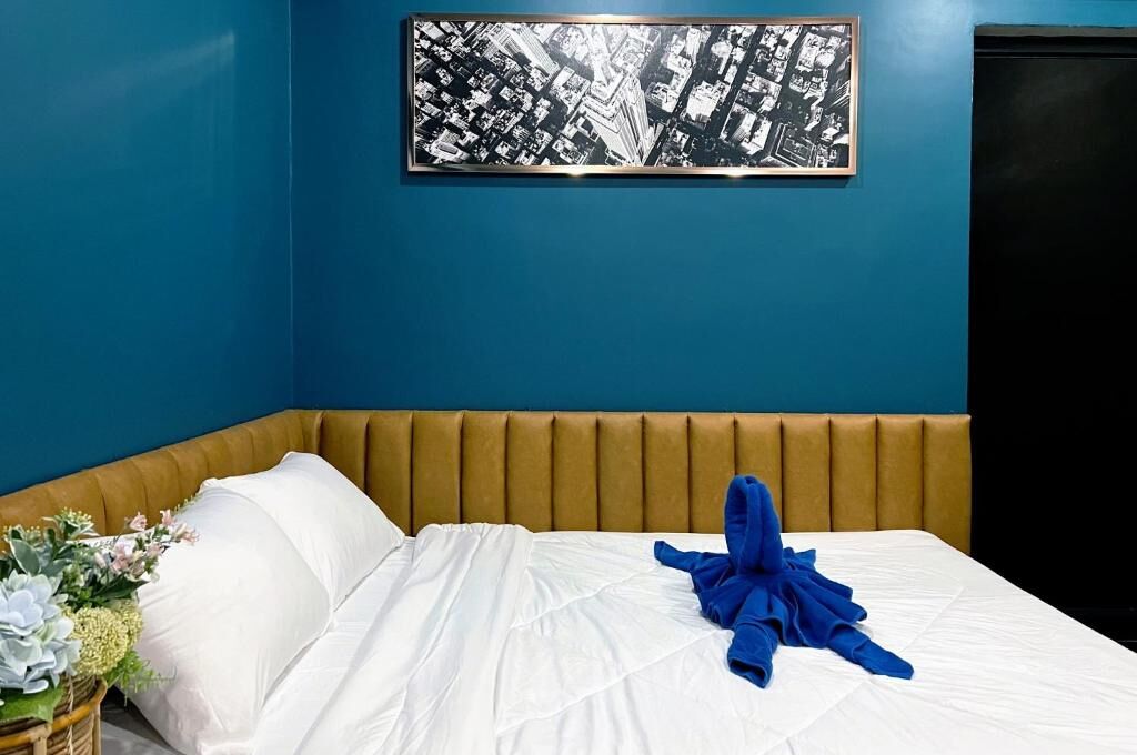 A hotel room with a bed, a headboard, a wall-mounted artwork, and a dark door.