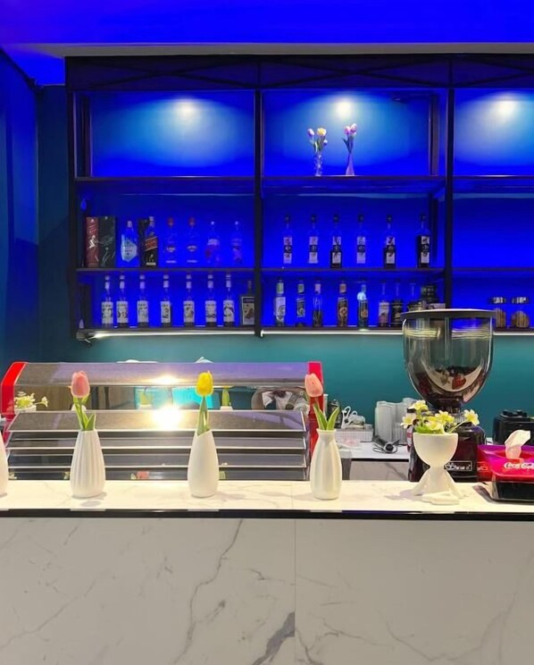 Un espace bar avec des étagères remplies de bouteilles d’alcool et des vases de fleurs disposés sur le comptoir.