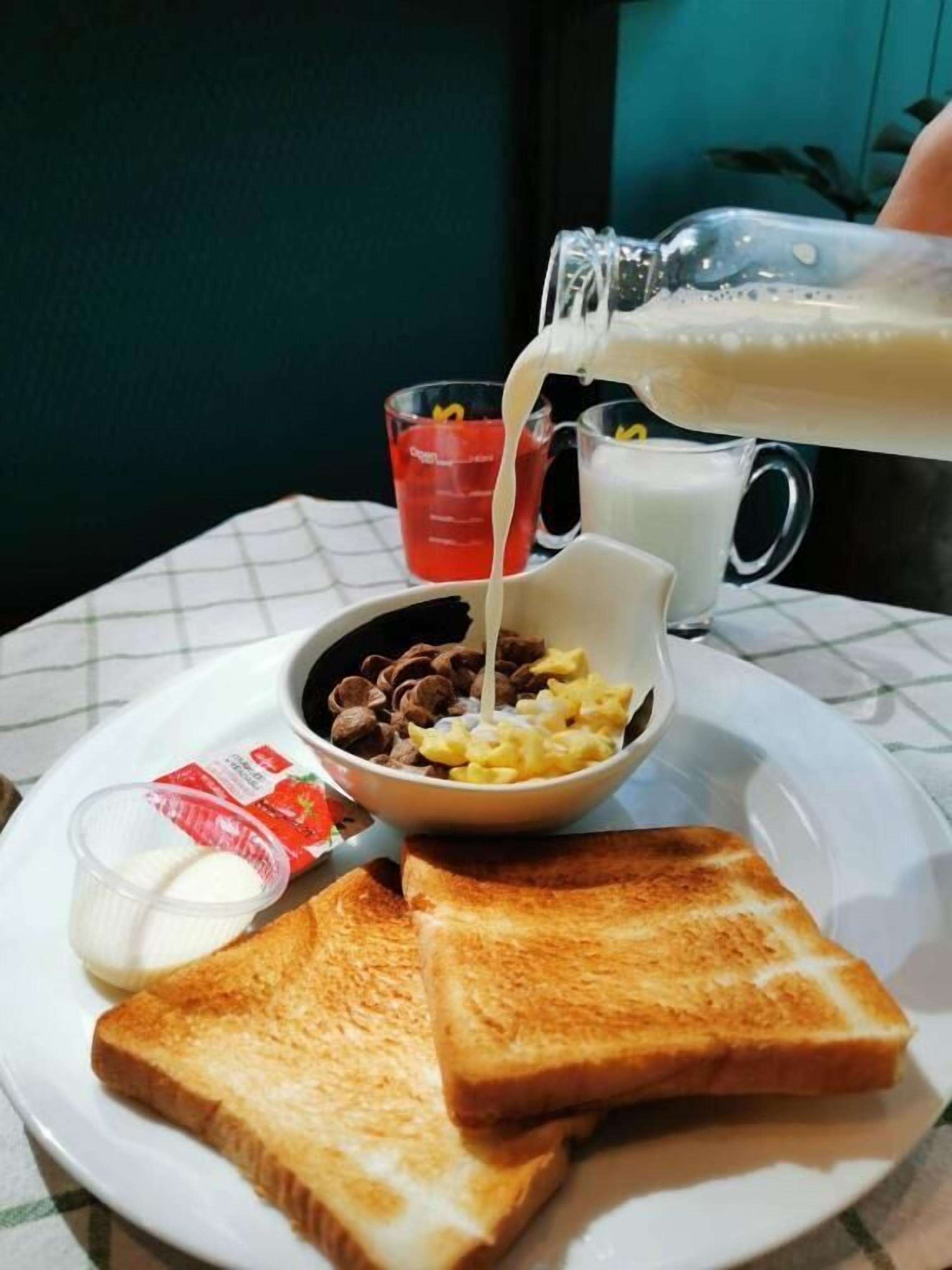 Piattino per la colazione con pane tostato, cereali e latte che viene versato.