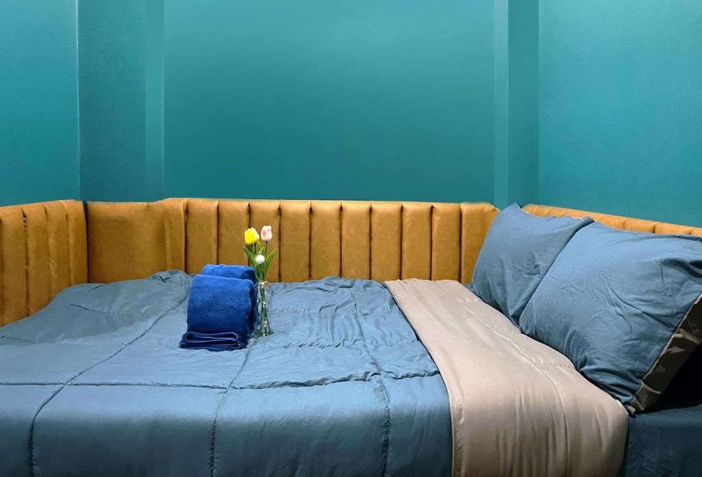 Un letto con una coperta blu, una trapunta beige e un piccolo vaso con fiori.
