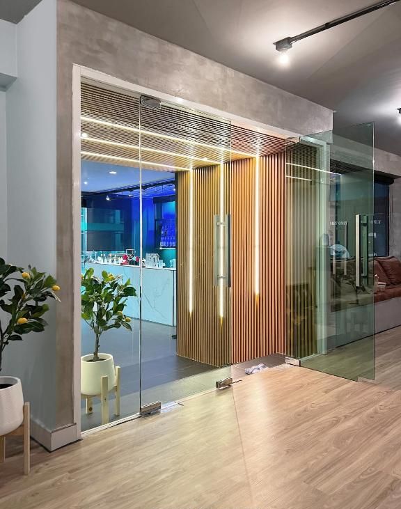 A modern interior with a glass partition, wooden slats, and a visible kitchenette area.