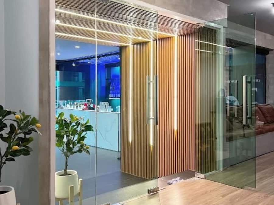 A modern interior with a glass partition, wooden slats, and a visible kitchenette area.