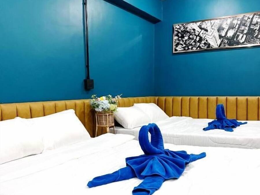 Une chambre d’hôtel avec deux lits, des murs bleus, une tête de lit en bois et une œuvre d’art représentant un paysage urbain en noir et blanc.