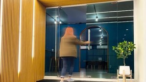 A person opening a sliding glass door at the entrance of a building with a modern design, featuring wooden slats and a dark interior. - Airport Mini Hostel at Don Muang Airport (Bangkok)