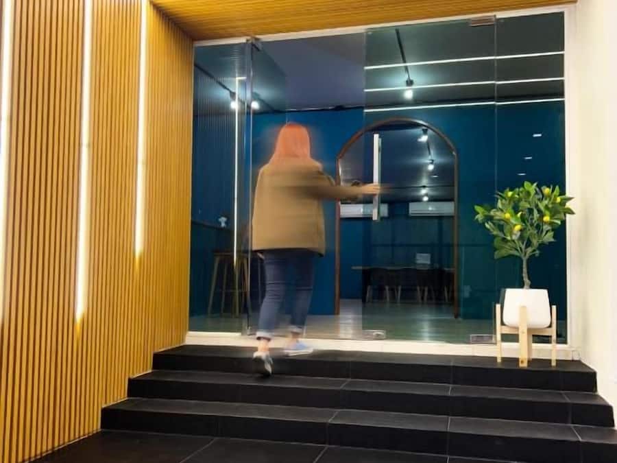 Iemand opent een schuifdeur bij de ingang van een gebouw met een modern ontwerp, met houten lamellen en een donker interieur.
