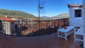 Una terraza con valla de bambú, mobiliario exterior blanco y vista a un paisaje montañoso.