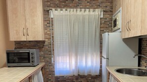 Una cocina compacta con pared de ladrillo, microondas, tostadora y pileta.