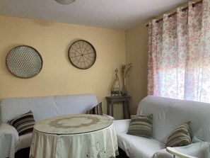 A living room with a sofa, a round table, decorative wall art, and a floral curtain. - CaMeme your house in the village (Cabrero)