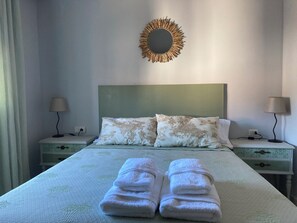 A neatly made bed with two pillows, a bedside table with a lamp, and a wall-mounted mirror. - CaMeme your house in the village (Cabrero)