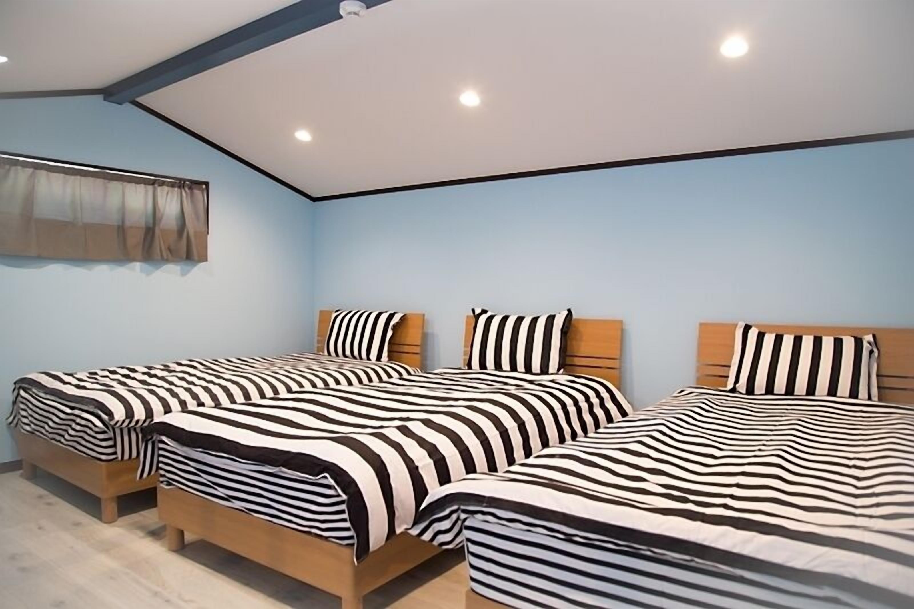 A room with three beds, each with striped bedding and wooden headboards.