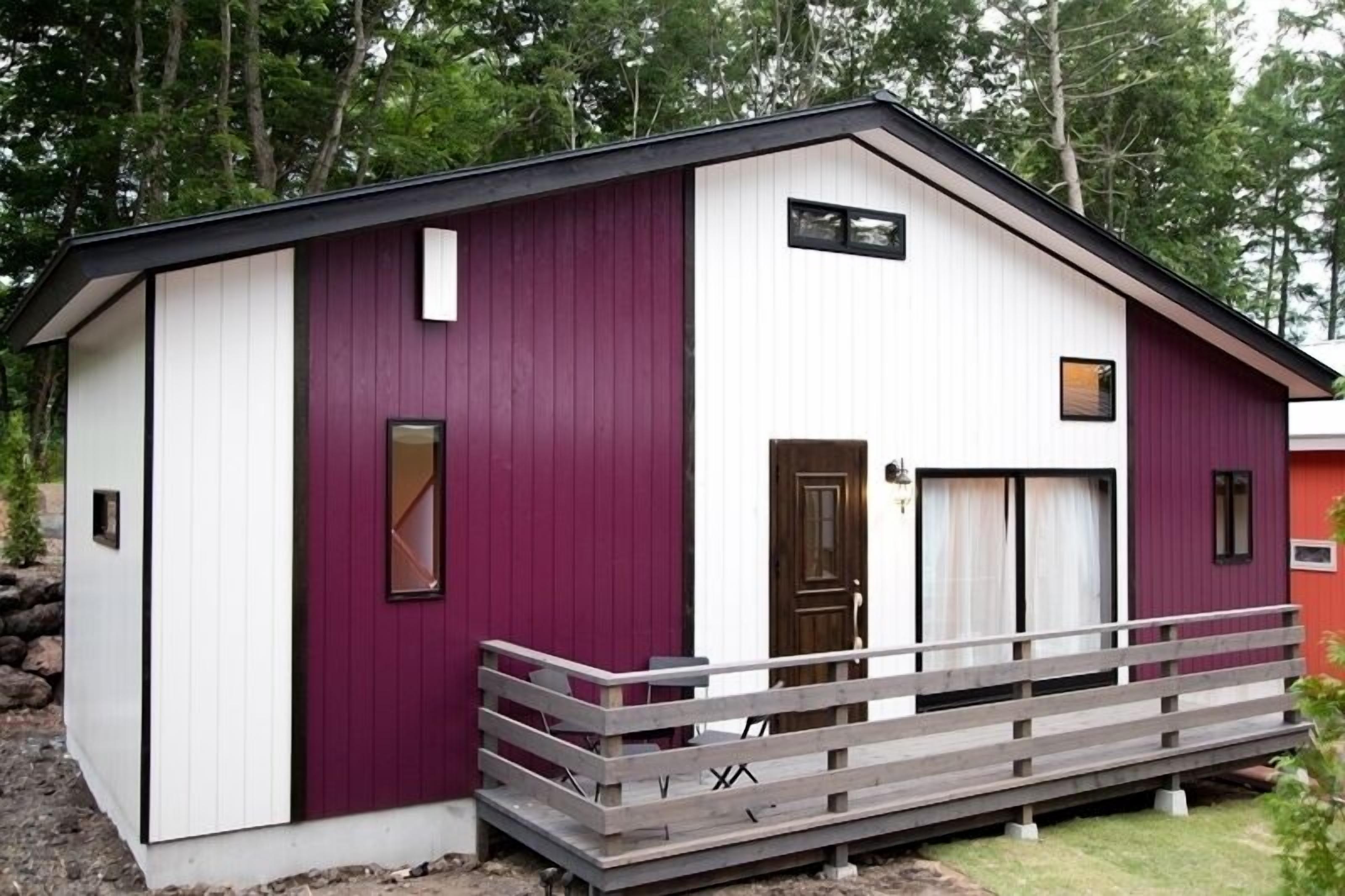 A small, single-story building with a purple and white exterior, a wooden front porch, and a door with a window.