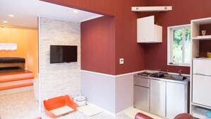 Un espace de vie compact comprenant un coin cuisine, un téléviseur à écran plat fixé sur un mur en pierre et une fenêtre laissant entrer la lumière naturelle.