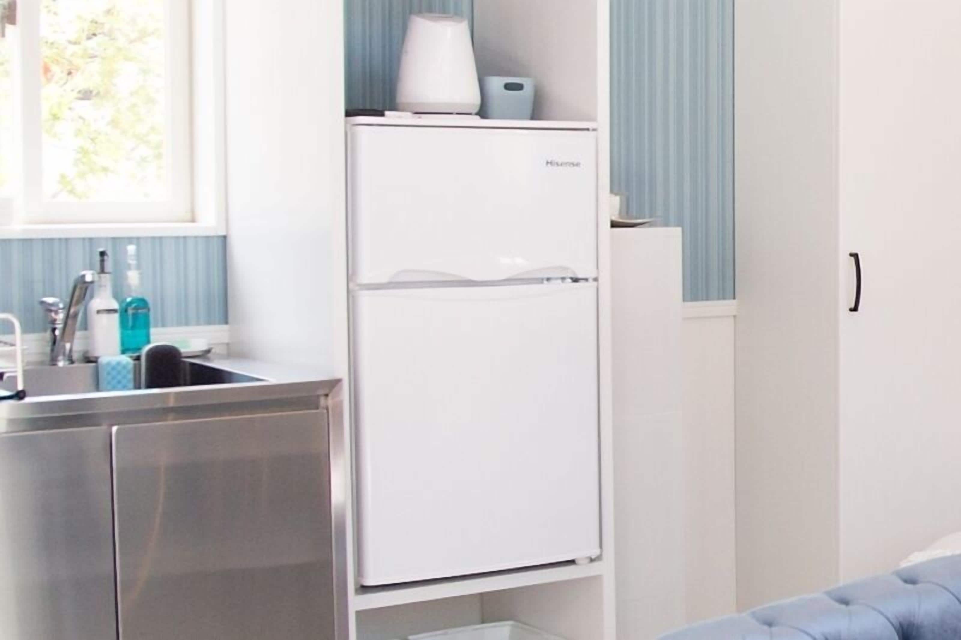 Una cocina compacta con un refrigerador blanco, un lavamanos y una ventana con cortinas.