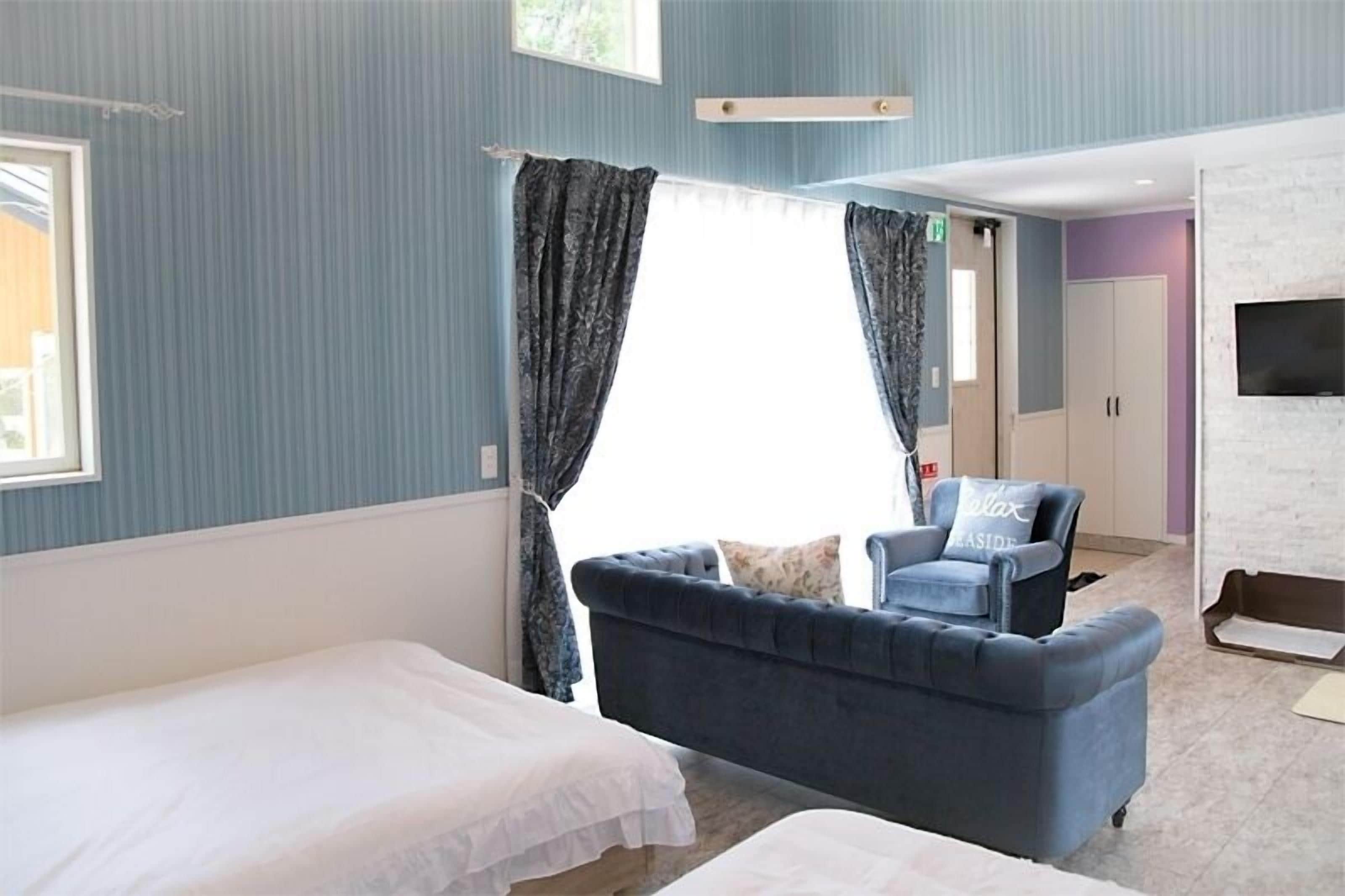 A room with two beds, a blue sofa, a TV, and a window with curtains.