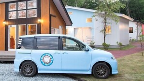 Un minibus bleu clair est garé devant un bâtiment moderne doté d’une façade en bois et de nombreuses fenêtres.