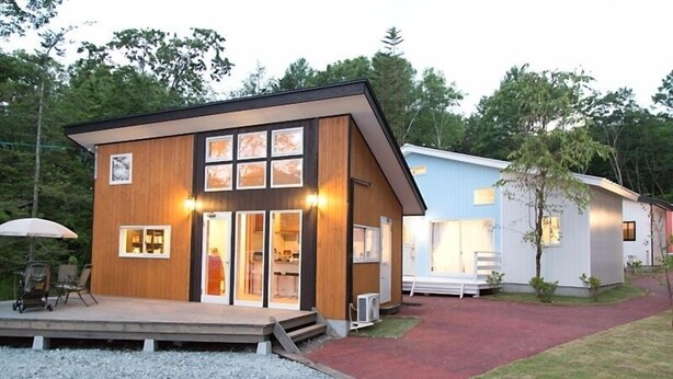 Une maison moderne à deux étages, avec une façade en bois, de grandes fenêtres et un patio couvert.
