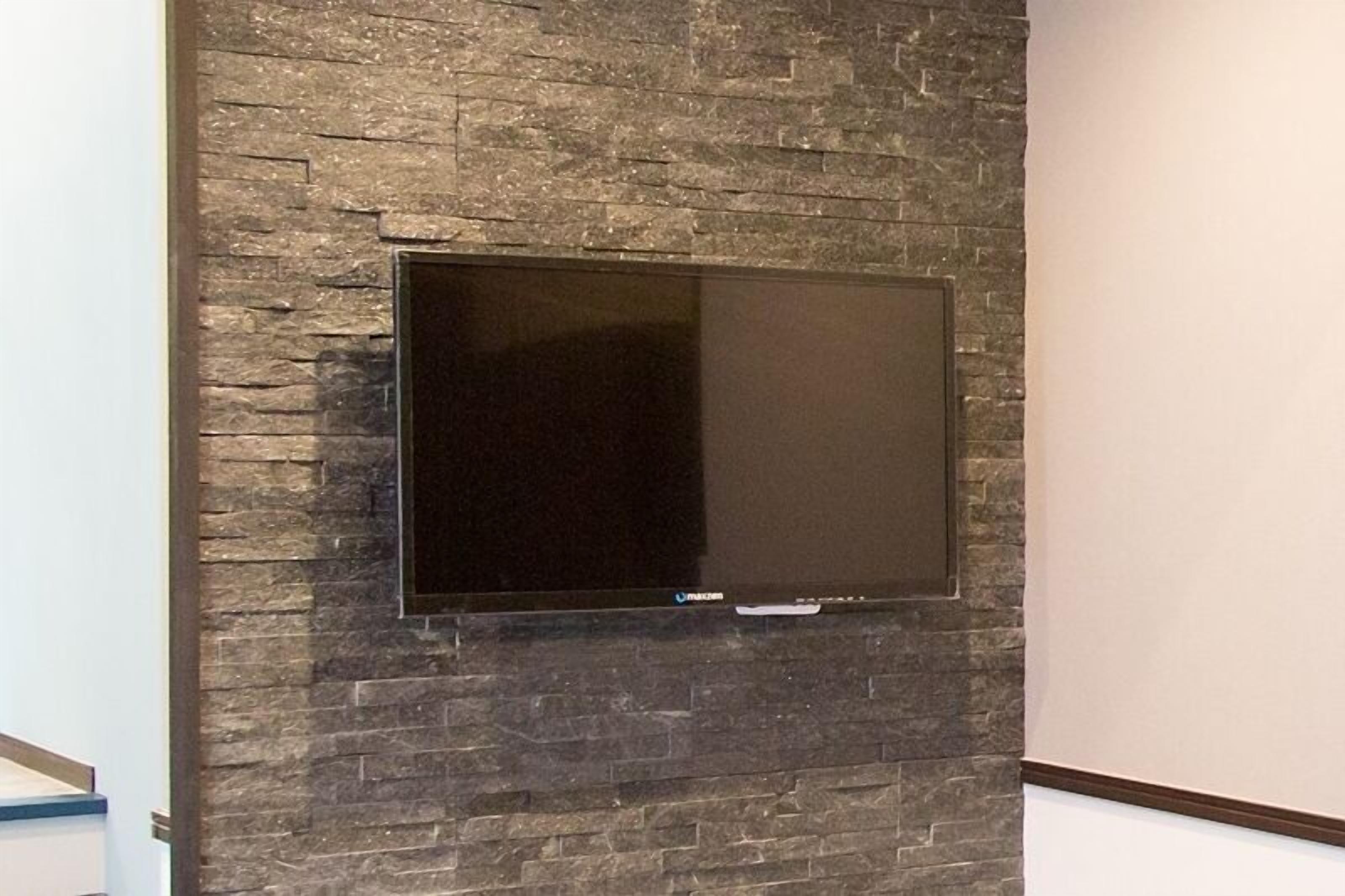 A flat-screen TV mounted on a textured stone wall.