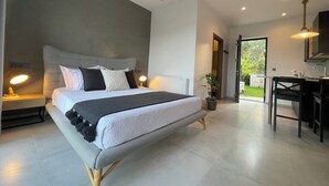 Un dormitorio moderno con una cama grande, lámparas de noche, una mesita y vistas al jardín a través de una puerta abierta.