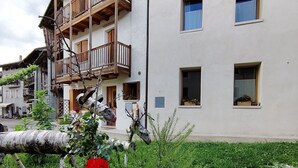 A building with multiple balconies, a garden with a red flower, and a stone pathway. - CasaZefira (Feltre)