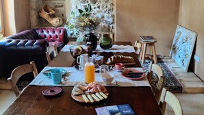 A rustic dining area with a stone wall, wooden furniture, and a variety of breakfast items on the table. - CasaZefira (Feltre)