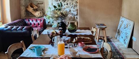 A rustic dining area with a stone wall, wooden furniture, and a variety of breakfast items on the table.