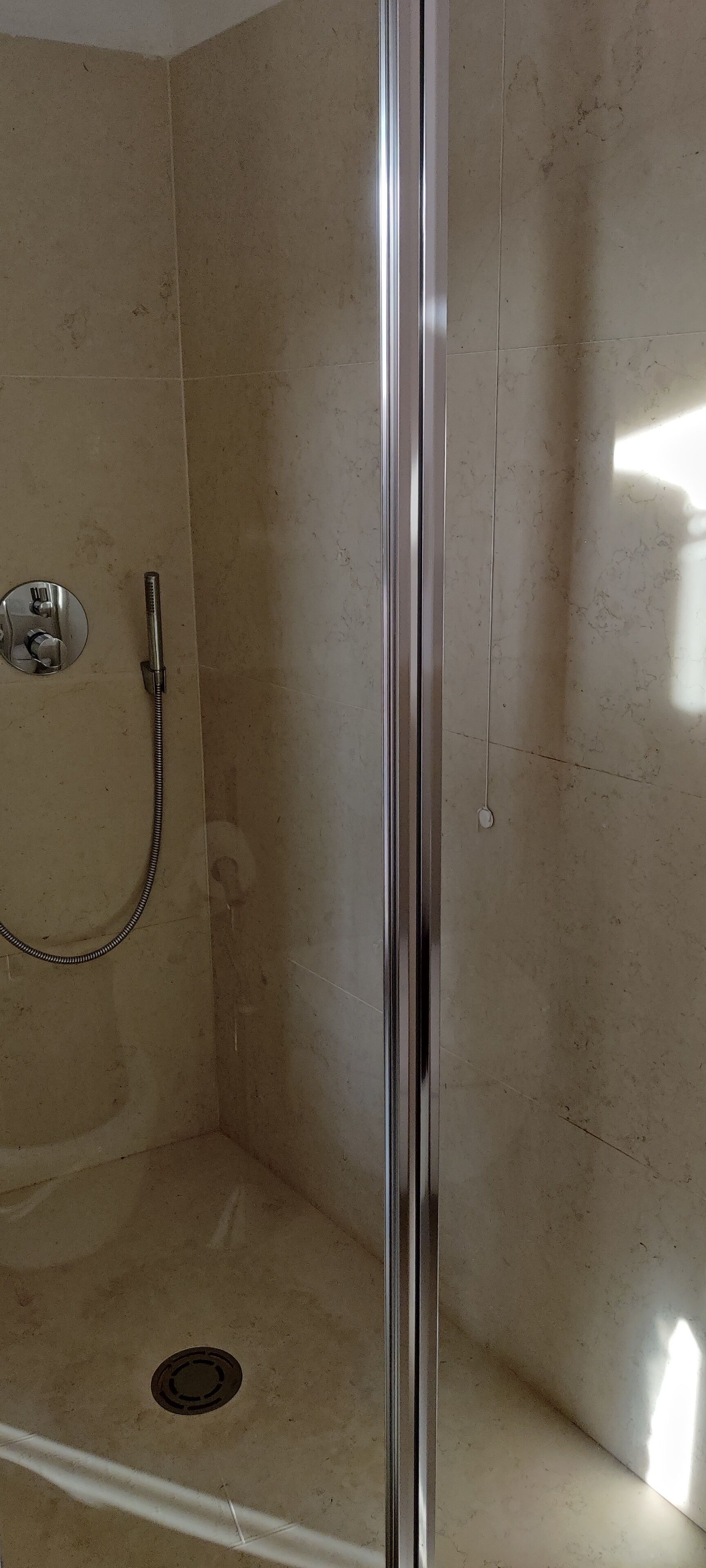 Een douche met een glazen deur, een handdouche en een wandmengkraan.