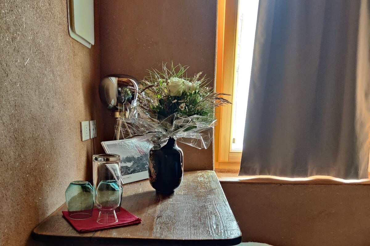 A small wooden table with a vase of flowers, a framed picture, and two glasses.
