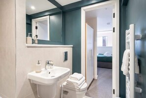 Une salle de bain moderne avec un lavabo, un miroir et des toilettes. On peut voir un porte-serviettes sur la droite.