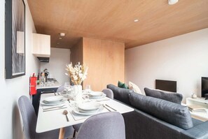 Un espace de repas moderne avec un plafond en bois, un canapé, un téléviseur et une cuisine en arrière-plan.