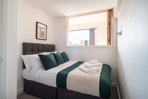 Une chambre d’hôtel avec un lit, une fenêtre, un tableau encadré au mur et une petite plante sur le rebord de la fenêtre.