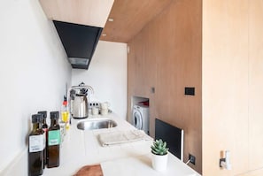 A compact kitchen with a sink, a coffee maker, and a washing machine. - Stunning 2 Bedroom Manchester Apartment w Balcony (Manchester)