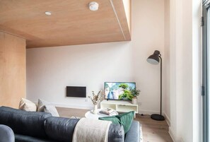A modern living room with a sofa, a coffee table, a TV, and a floor lamp. - Stunning 2 Bedroom Manchester Apartment w Balcony (Manchester)