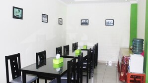 Un comedor con una mesa larga y varias sillas, cuadros en las paredes y un dispensador de agua a la derecha.