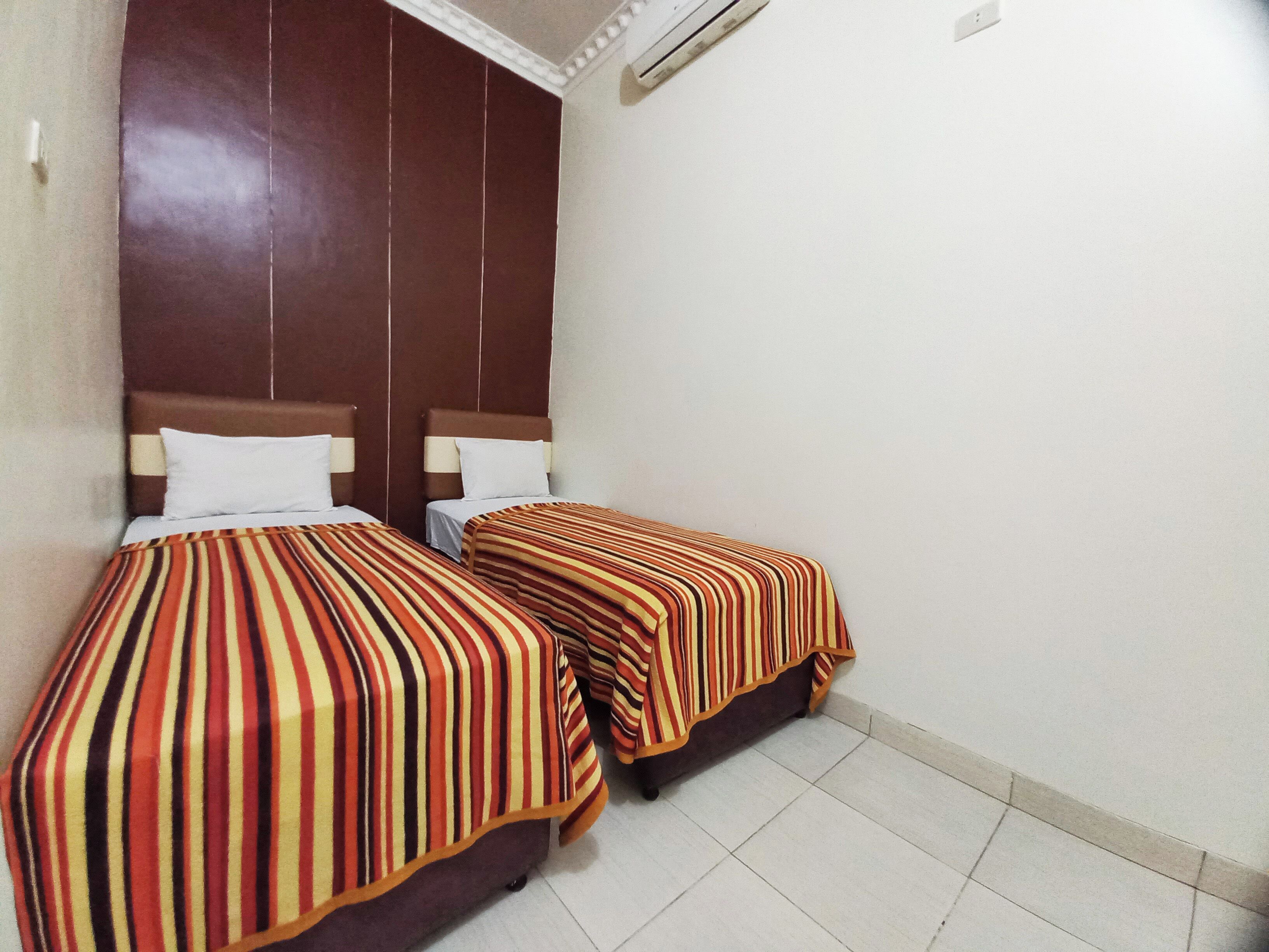 Ein Hotelzimmer mit zwei Betten, jeweils mit gestreifter Bettwäsche, Holz-Kopfteilen und einer weißen Wand.