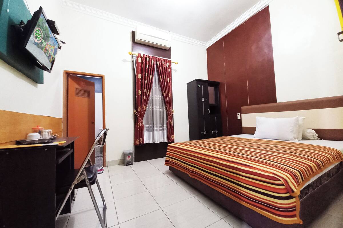 A hotel room with a bed, a desk, a chair, an air conditioning unit, a wardrobe, and a television on the wall.