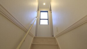 A narrow staircase with wooden steps and a handrail, leading to a small window at the top.