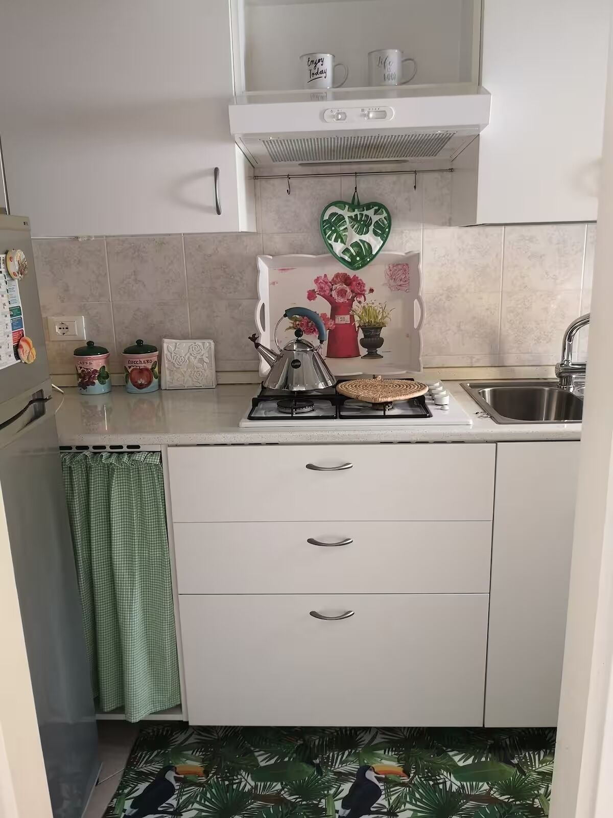 Uma cozinha com armários brancos, fogão a gás, pia e uma decoração de coração na parede.