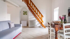 A modern living room with a grey sofa, a wooden staircase, a dining table with chairs, and a radiator. - LOVELY APARTMENT IN AN ANCIENT HAMLET WITH LAKE VIEW AND PATIO (Marone)
