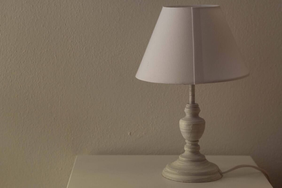 Una lampada da tavolo bianca con un paralume conico su un tavolo bianco, su uno sfondo neutro.