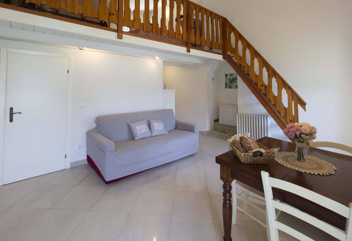 Ein Wohnzimmer mit einer Couch, einem Esstisch mit Stühlen und einer Holztreppe.