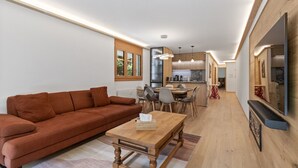 A modern living room with a brown sofa, wooden coffee table, and dining area with chairs and a kitchen in the background.
