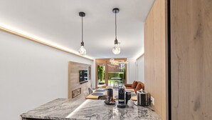 A modern kitchen with a marble countertop, two pendant lights, and a view of a dining area with a table and chairs.