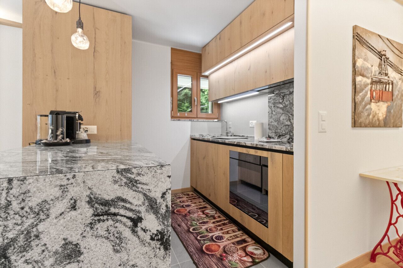 A modern kitchen with a marble island, wooden cabinets, and a red chair.