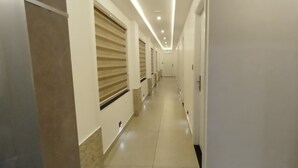 Um corredor comprido e estreito, com paredes brancas e chão de azulejos.